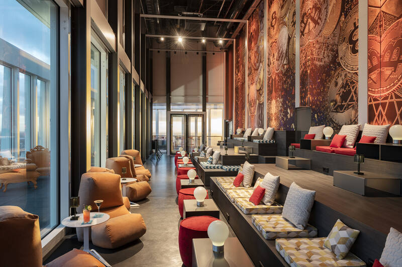 Modernes Lounge-Interieur mit gestuften Sitzbereichen, bunten Kissen und großen Fenstern mit Blick auf die Stadt