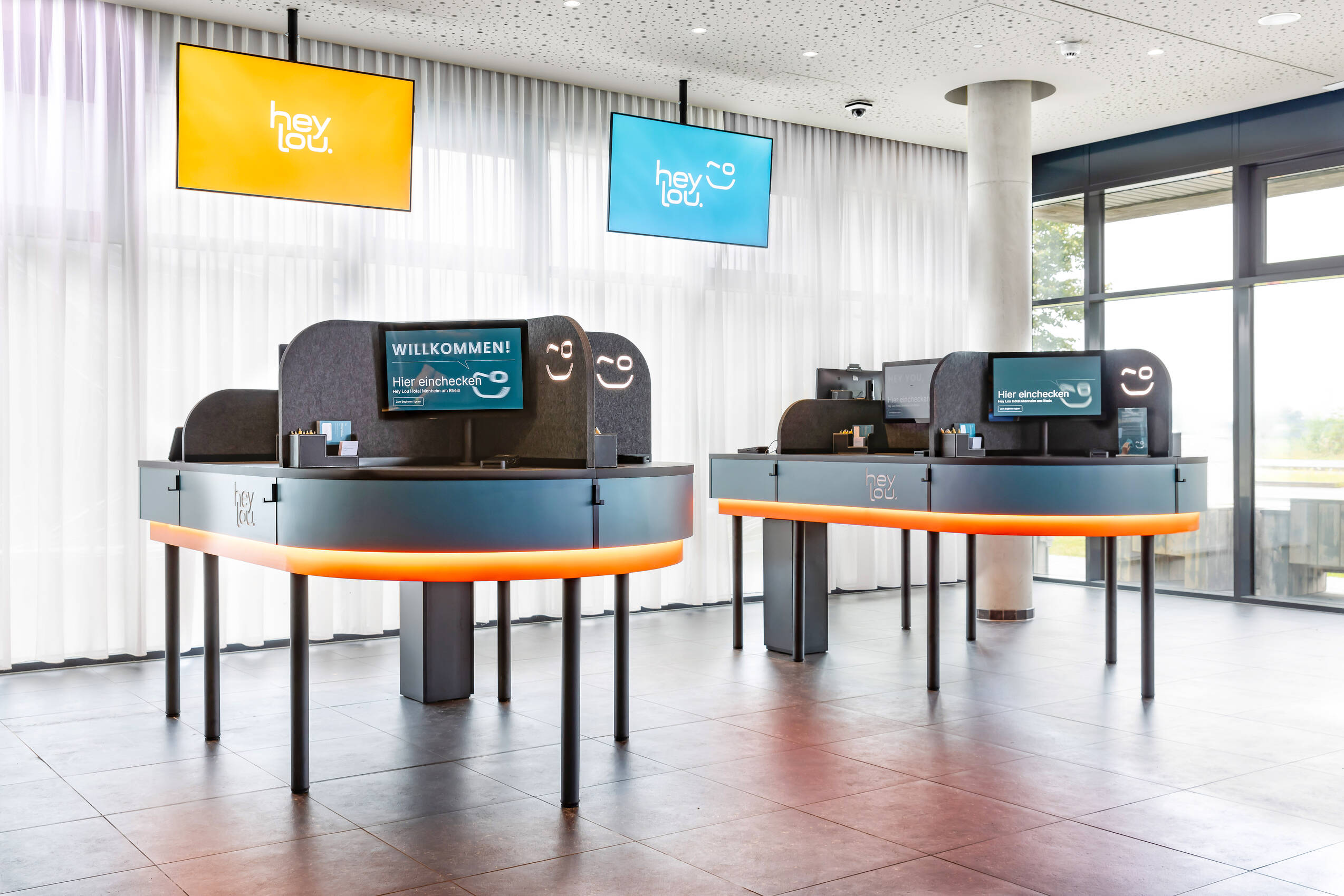 Digitaler Check-in Bereich mit Welcome Desk mit mehreren Bildschirmen und Leuchtschildern, die Begrüßung und KI-Optimierung anzeigen