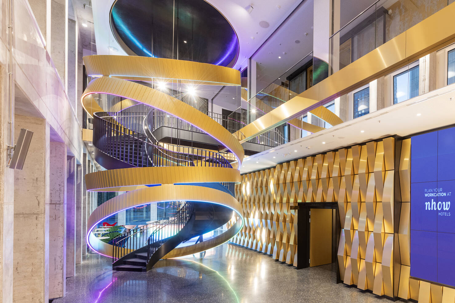 Moderner Innenraum mit spiralförmiger Treppe und goldfarbenen Wandpaneelen und aufwändiger Beleuchtung im nhow Hotel