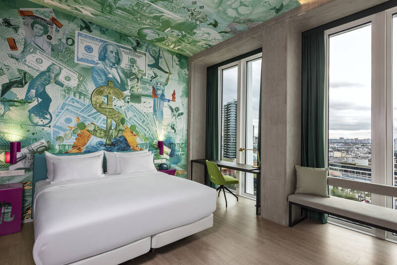 Hotelzimmer mit großem Bett vor einer Wand mit Wandbild aus US-Dollar-Scheinen und Gold-Dollarzeichen, zwei großen Fenstern mit Blick auf Stadt
